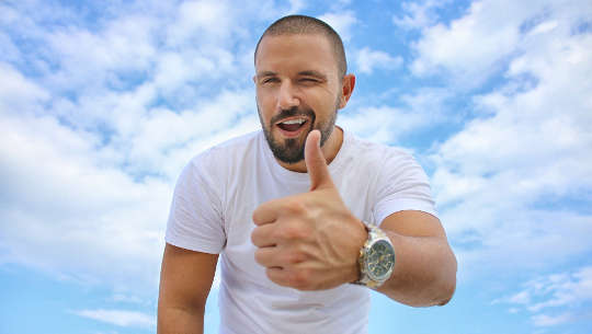 man with a "thumbs up" with sky and clouds in the background