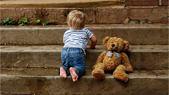 child crawling up some steps with his teddy bear