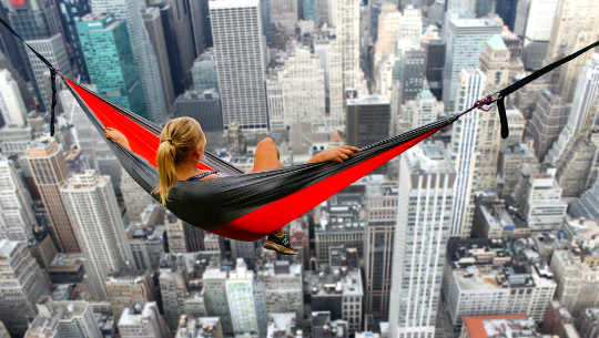 girl in a hammock hanging over the skyline of big city skyscrapers