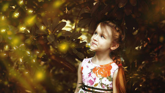 young girl looking up at fireflies in the sky