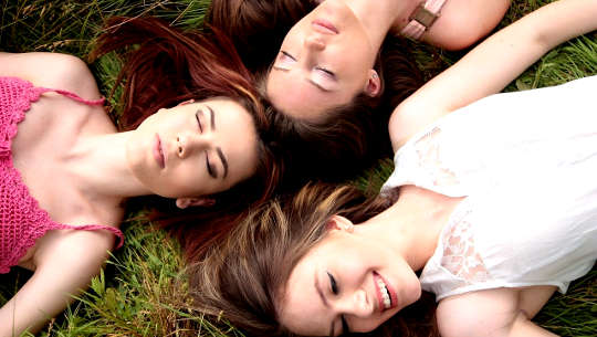 three young women, smiling, laying on their back outside