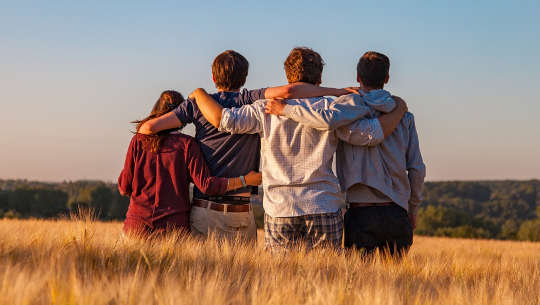 4 young adults sitting together with their arms linked over their shoulders - seen from the back