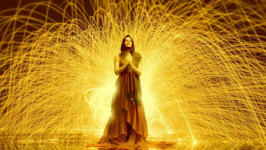a woman standing with hands in prayer position with rays of light streaming out from her