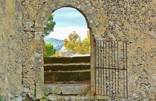 An open gate in a stone wall, opening up to a beautiful nature scene.
