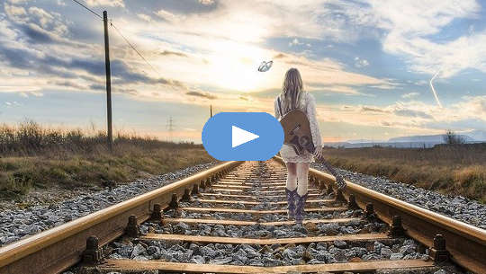 Girl with a guitar on her back walking down the railroad tracks.