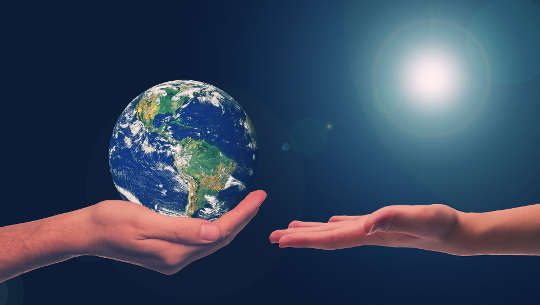 two hands, one holding the earth, the other hand open to receive