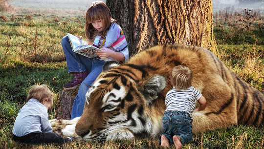 young girl reading a book and sitting next to a tiger and two very young children
