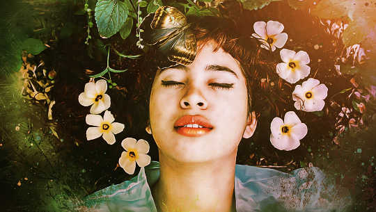 a woman laying down in nature with eyes closed and flowers in her hair