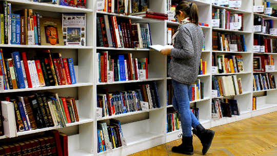 girl standing looking at a book in front of shelves in a bookstore