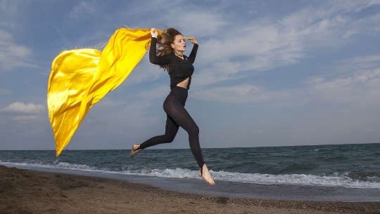 woman running down the beach with a cape flying in the wind behind her