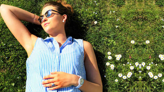 smiling woman lying back in the grass with yes closed