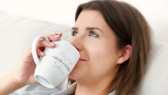woman drinking from a cup with a contented look upon her face