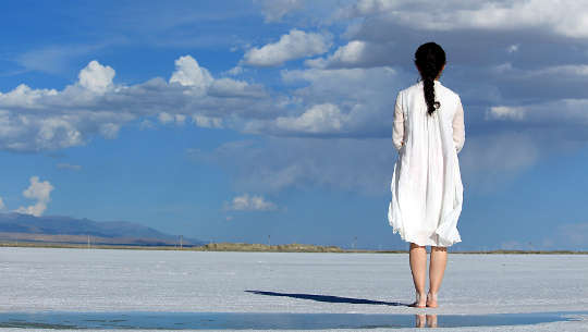 girl standing barefoot on a beach looking out at the great beyond
