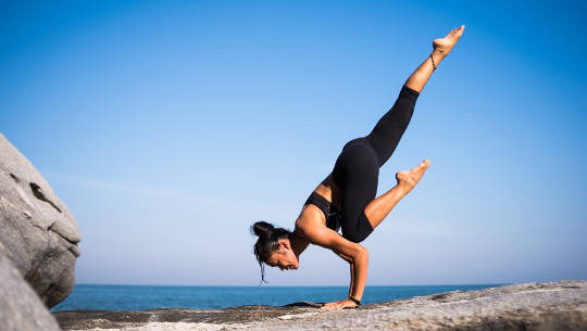 woman balanced on her hands in a yoga pose on the beach