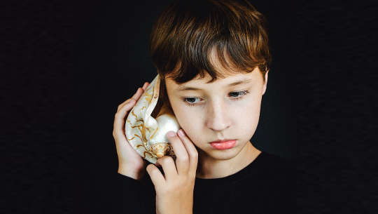 younf girl holding a seashell to her ear