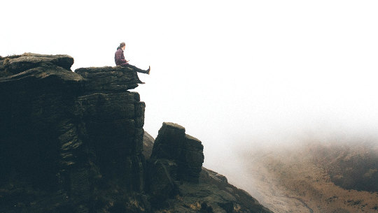 person sitting on the edge of a cliff dangling their legs over the edge