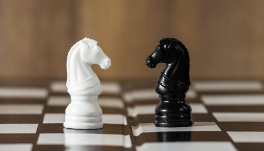 two chess pieces, a white knight and a black knight, facing each other on a chess board