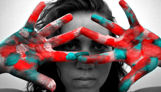 young woman looking through her multi-colored painted hands