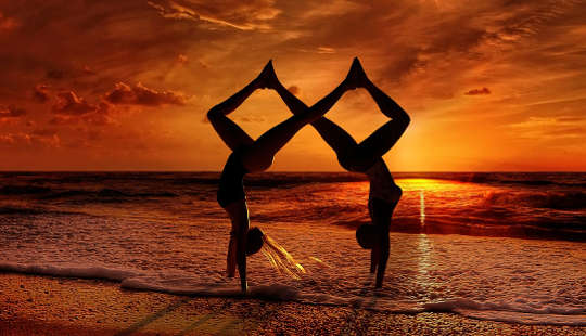 two people doing a combined yoga posture on a beach