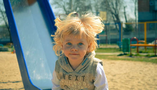 a child at the bottom of a slide with her hair in all directions