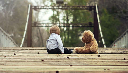 young boy sitting on a bridge with his teddy bear