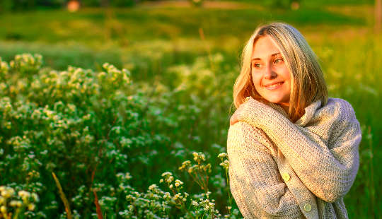 a smiling woman in a field of flowers giving herself a hug